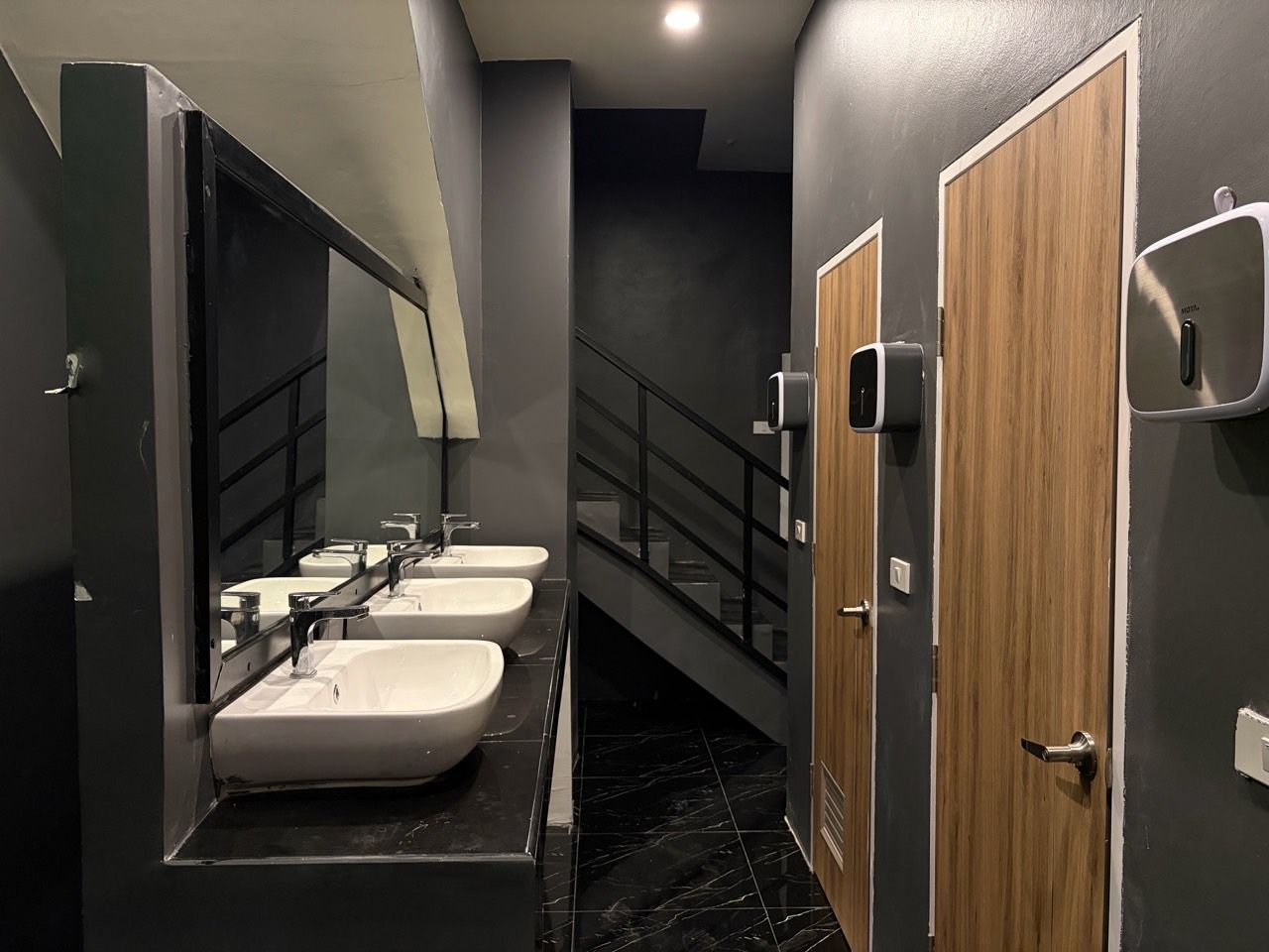 A public restroom with three sinks, a mirror, and a wooden door.