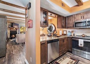 A modern kitchen with wooden cabinets, stainless steel appliances, and a stone fireplace. - Mountain Bear Retreat (Gatlinburg)