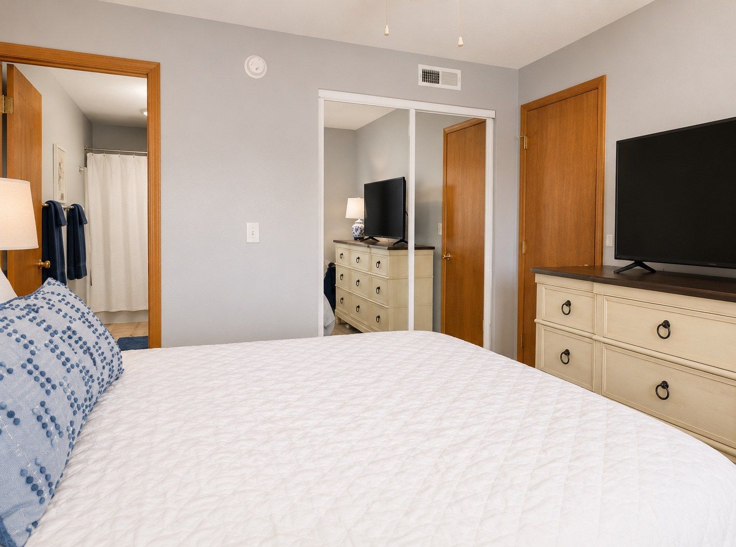 A bedroom with a bed, a dresser, a television, and a mirror.