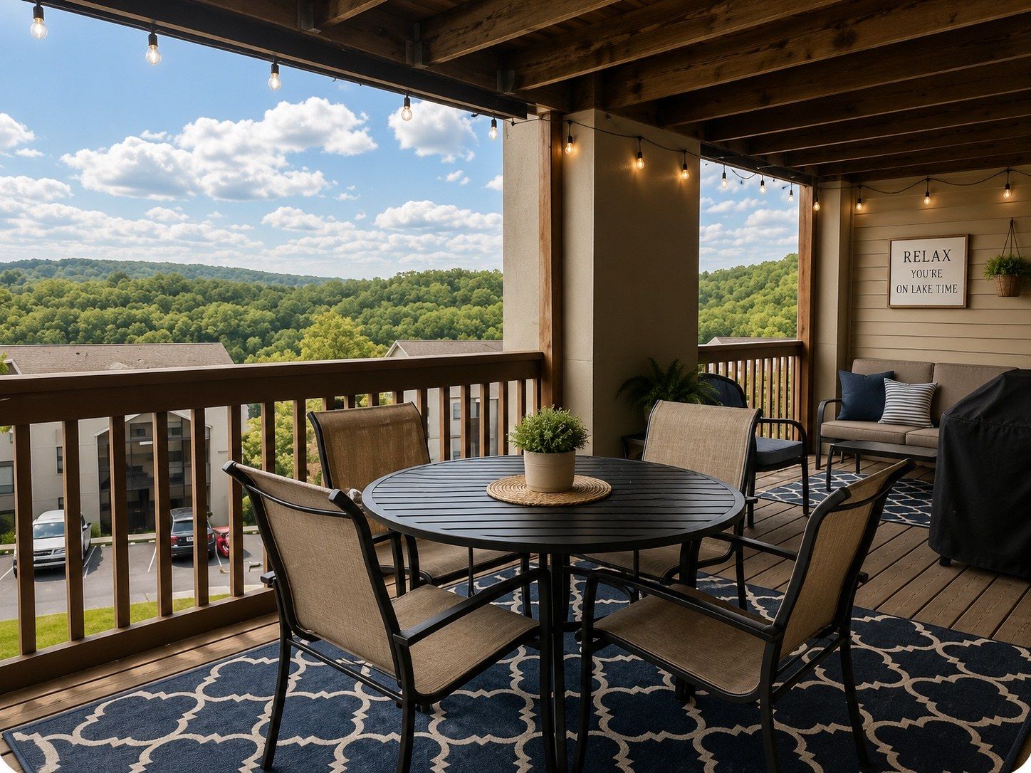 A covered outdoor seating area with a table and chairs, a view of a forested hill, and a sign that reads 'RELAX YOU'RE ON LAKE TIME'.