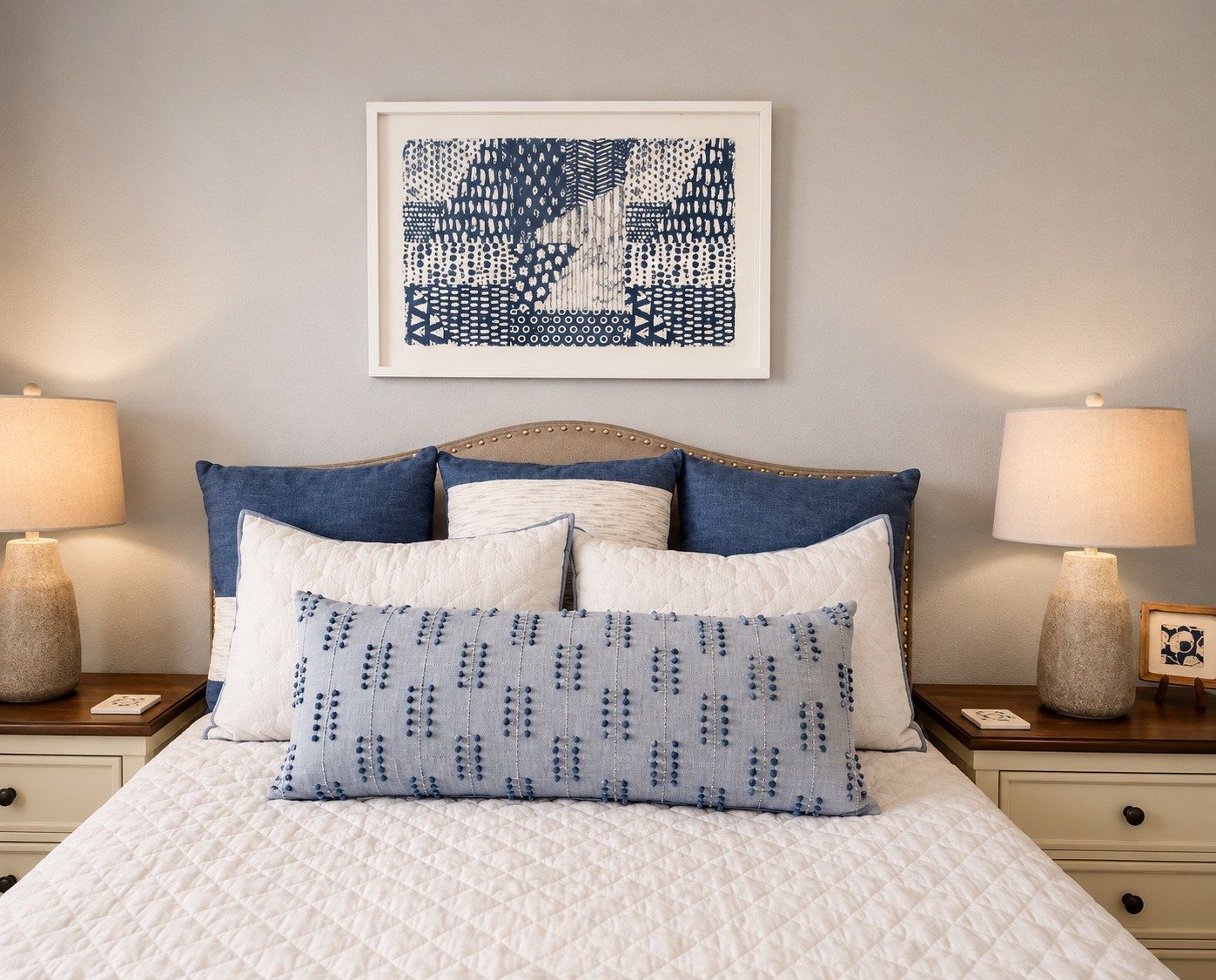A neatly made bed with a quilted white cover, flanked by two nightstands with lamps and a framed artwork above.
