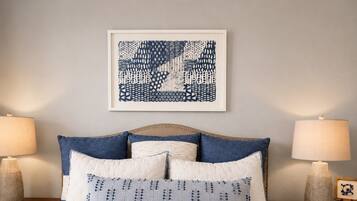A neatly made bed with a quilted white cover, flanked by two nightstands with lamps and a framed artwork above.