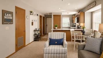 A spacious living area with a striped armchair, a sofa, a dining table, and a kitchen in the background.