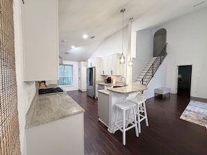 A modern kitchen with a central island, stainless steel appliances, and a staircase leading to an upper level. - Luxury Coastal Retreat/Private Pool/Lanai/Fire Pit/ Community Pool (Destin)
