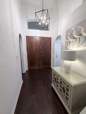 A hallway with a wooden door, a white console table with a lamp, and a geometric chandelier. - Luxury Coastal Retreat/Private Pool/Lanai/Fire Pit/ Community Pool (Destin)