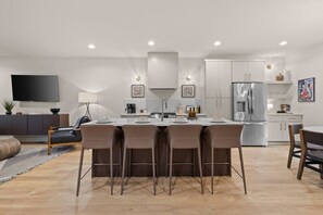 A modern kitchen with a central island, stainless steel appliances, and a dining area with a sofa and chairs. - Chic Townhome in East • Rooftop • Garage • Near Downtown (Nashville)