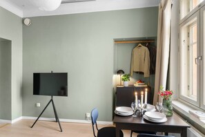 Ein Zimmer mit einem Flachbildfernseher auf einem Stativ, einem Esstisch mit Kerzen, Tellern und Gläsern sowie einem Fenster mit Vorhängen.
