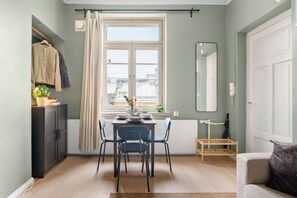 Un coin repas avec une table dressée pour deux personnes, une fenêtre avec des rideaux, un miroir et un radiateur.