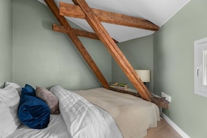 A bedroom with a sloped ceiling, a bed with white bedding, and a bedside table with books. - 1875 Attic | Bathtub | Walking Street | Top Floor (Helsinki)