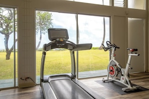 A home gym with a treadmill and an exercise bike, large windows with a view of a lawn and trees. - Cozy 1-bedroom apartment with AC in serene Hauula (Hauula)