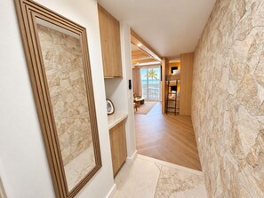 A hallway with a stone wall, wooden flooring, and a view of a balcony with a palm tree. - Cozy 1-bedroom apartment with AC in serene Hauula (Hauula)