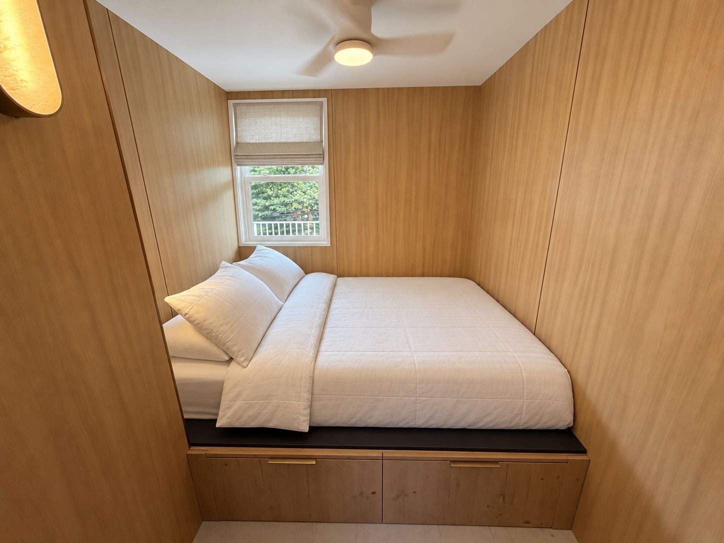 A compact room with a bed, a window with a view, and a ceiling fan.