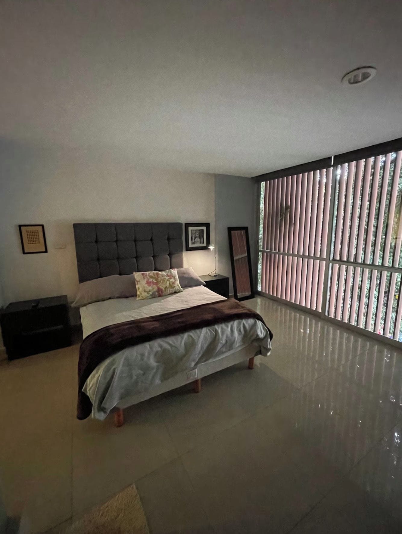 Ein Schlafzimmer mit einem großen Bett, einem Nachttisch, einer Fensterbank und einem Fenster mit Jalousien.