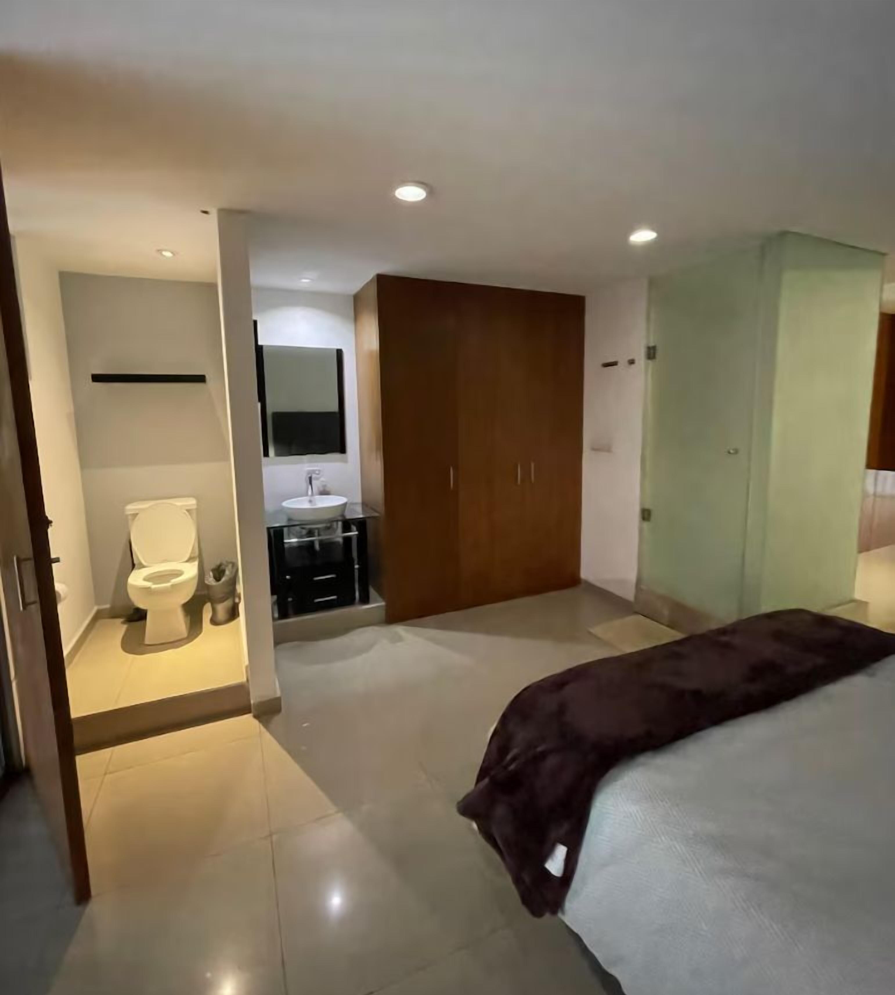 Ein Schlafzimmer mit Bett, Kleiderschrank, Badezimmer mit Toilette und Waschbecken sowie einem Spiegel.