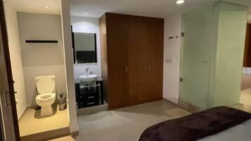 Ein Schlafzimmer mit Bett, Kleiderschrank, Badezimmer mit Toilette und Waschbecken sowie einem Spiegel.