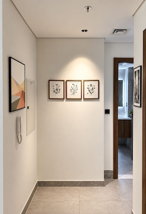 A hallway with a phone, three framed botanical prints on the wall, and a door leading to a bathroom.