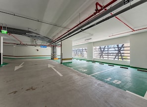 Ruime parkeergarage met pijlen op de vloer, een groen uitgangsbord en een zicht op buiten via grote ramen.
