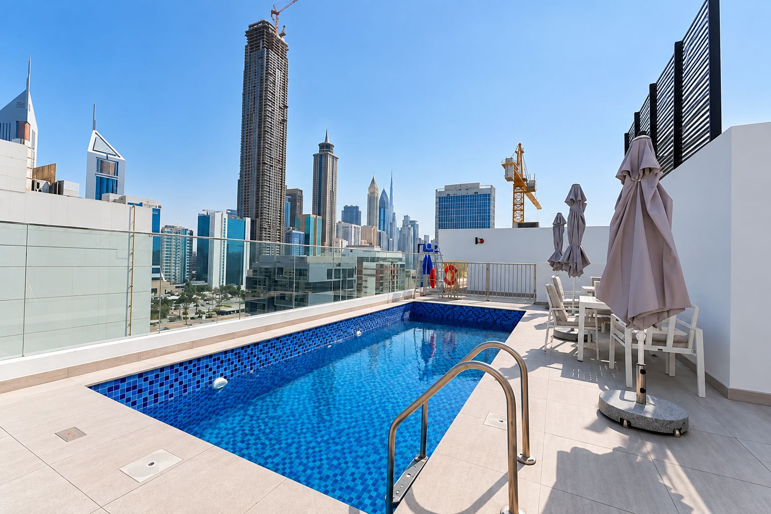 Una piscina en la azotea con vista al horizonte urbano, barandilla de cristal y mobiliario exterior con sombrillas.