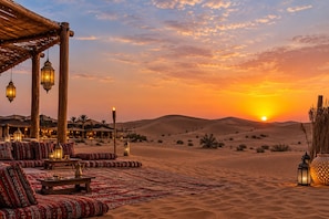 Paisaje desértico con atardecer, un espacio de descanso con cojines estampados y faroles tradicionales.