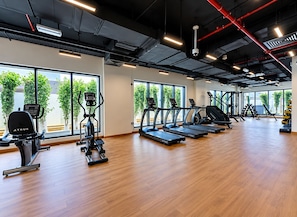 Un gimnasio con máquinas de cardio, pesas y un amplio ventanal con vistas a árboles.