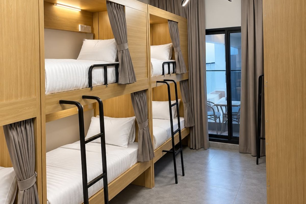 Een hotelkamer met stapelbedden, een plafondlamp, een raam met gordijnen en uitzicht op het omliggende landschap.