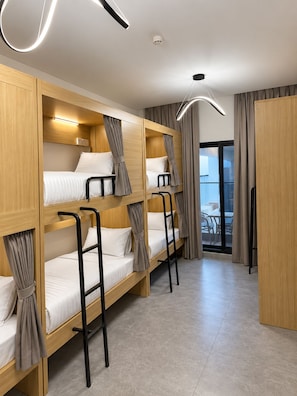Een hotelkamer met stapelbedden, een plafondlamp, een raam met gordijnen en uitzicht op het omliggende landschap.