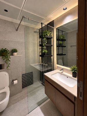 Een moderne badkamer met een douchecabine van glas, een witte wastafel en meerdere planken met potplanten.