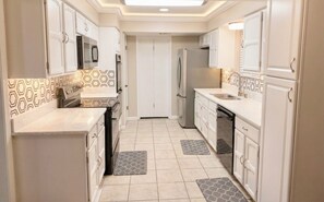 A compact kitchen with white cabinets, a microwave, a refrigerator, and patterned backsplash tiles. - Tremendous 4-bedroom house with all amenities (Kenner)