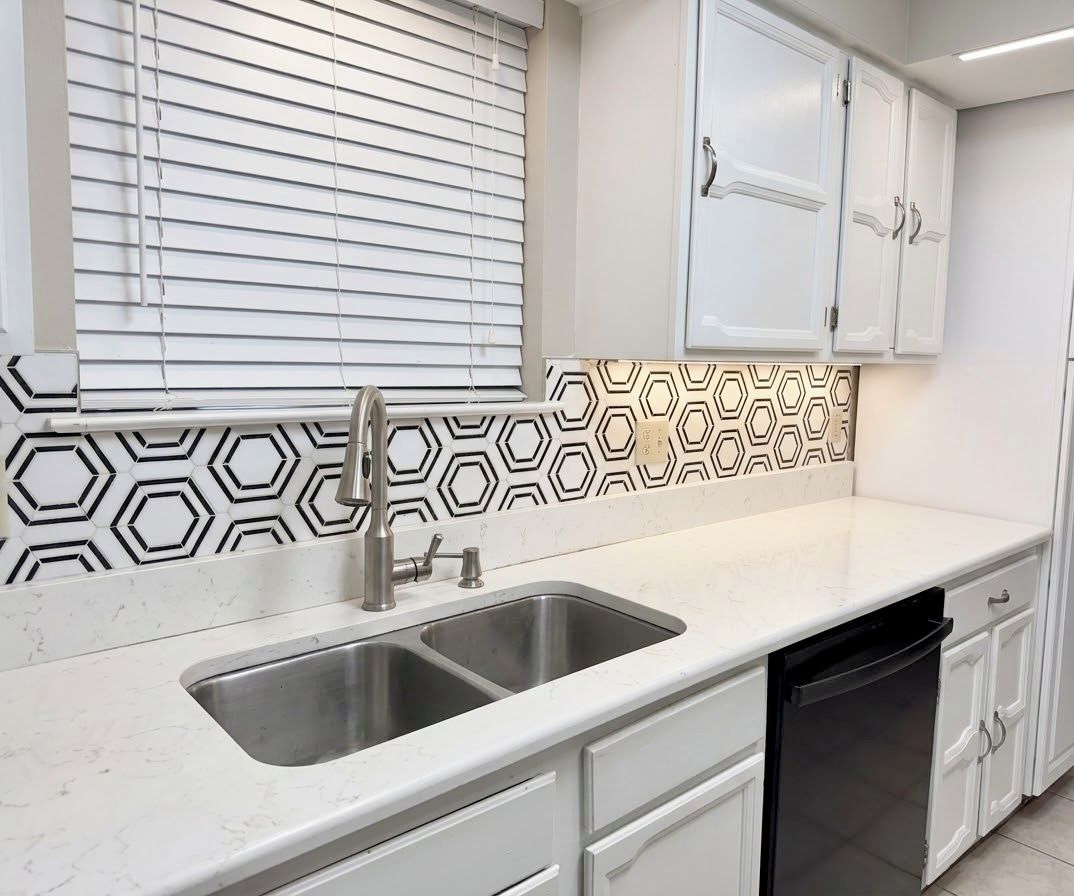 Et køkken med en dobbeltvask, hvide skabe og et mønstret backsplash.