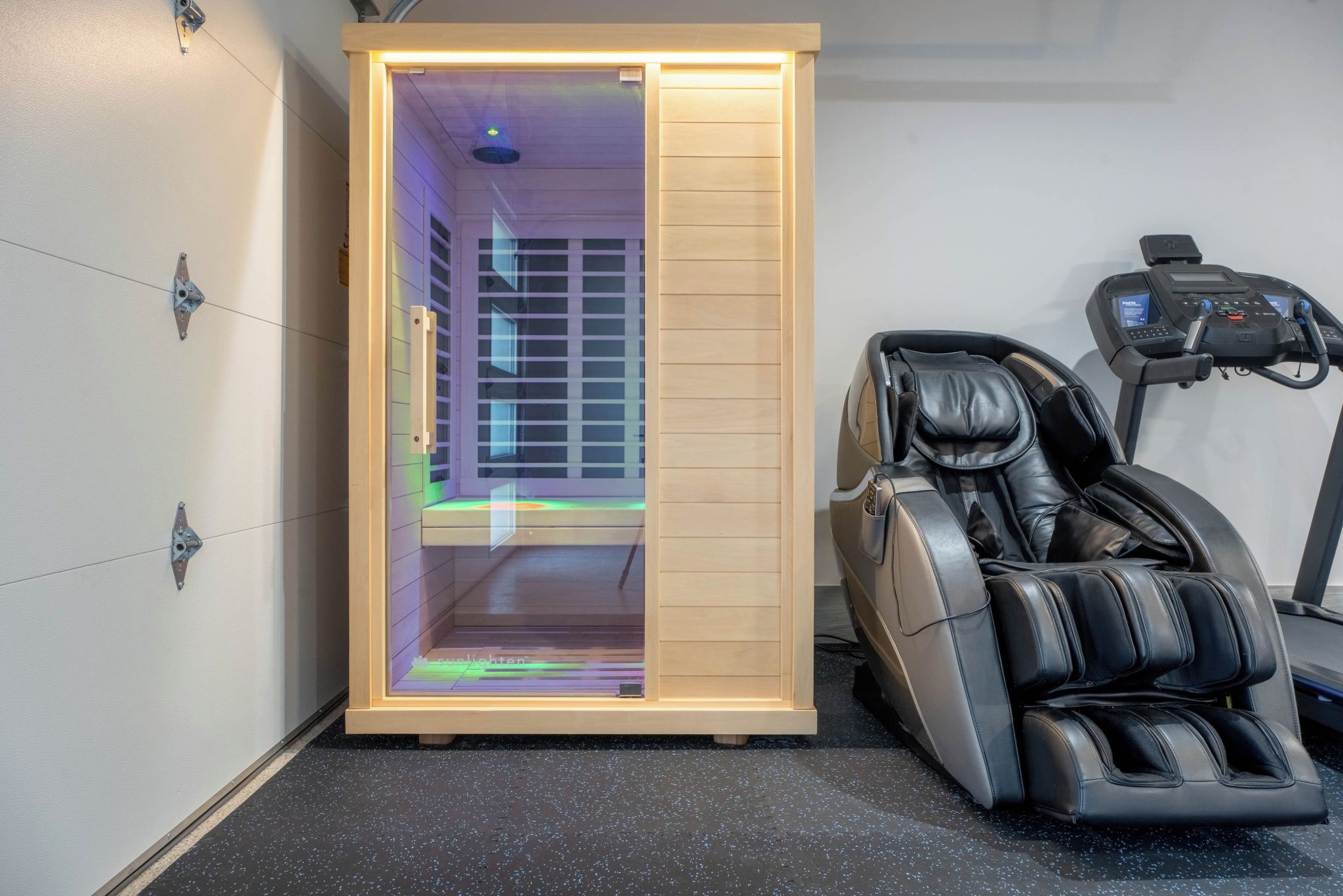 A sauna room with a wooden door, a massage chair, and a treadmill.