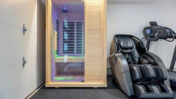 A sauna room with a wooden door, a massage chair, and a treadmill.