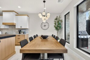 Una cocina moderna con una mesa de comedor de madera, sillas negras, una lámpara colgante y un reloj de pared grande.