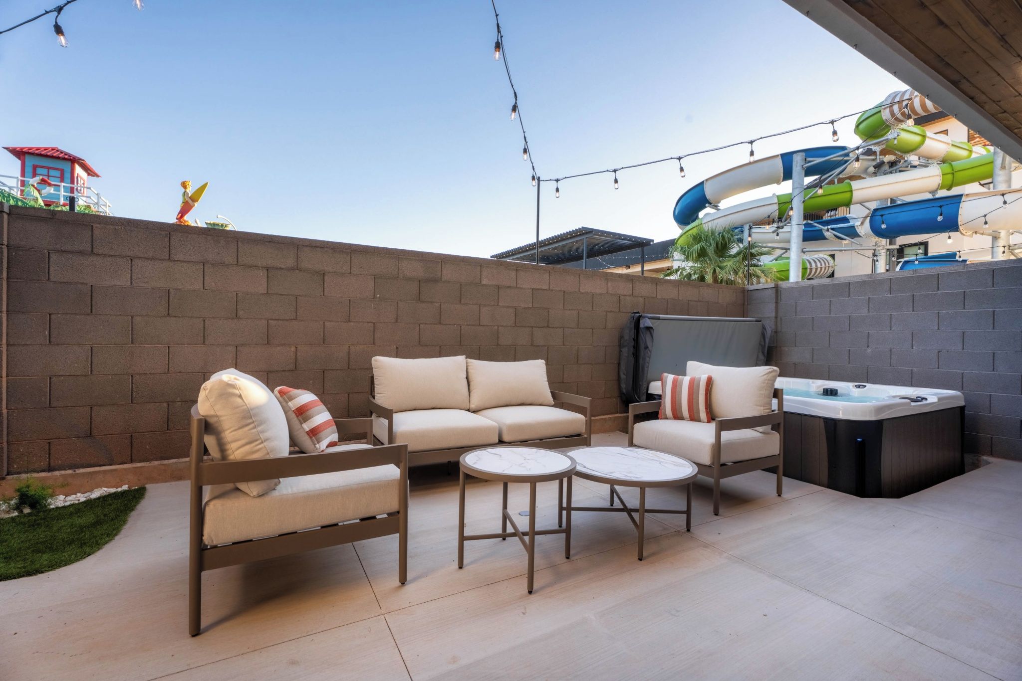 An outdoor patio with a sofa set, two round tables, and a hot tub.
