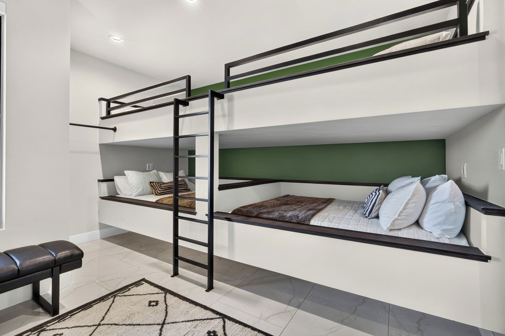A bunk bed room with a ladder, a bench, and a patterned rug.