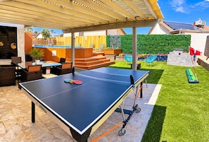 An outdoor ping pong table with a covered seating area, a pool, and a well-maintained lawn. - 4-Bedroom Home • Pool • BBQ • Ping Pong • Near the Strip (Henderson)