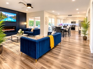 A modern living room with a flat-screen TV, a fireplace, and a dining area with a kitchen in the background. - 4-Bedroom Home • Pool • BBQ • Ping Pong • Near the Strip (Henderson)