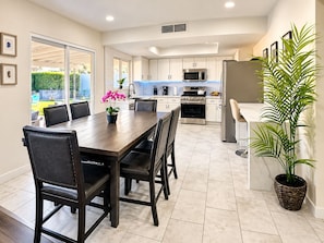 A modern kitchen with white cabinets, stainless steel appliances, and a dining area with a wooden table and chairs. - 4-Bedroom Home • Pool • BBQ • Ping Pong • Near the Strip (Henderson)