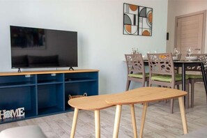 A living room with a TV, blue storage units, a dining table with chairs, and a bench. - Beachside • Balcony • Estoril Beach • Best Beach (Sal Rei)