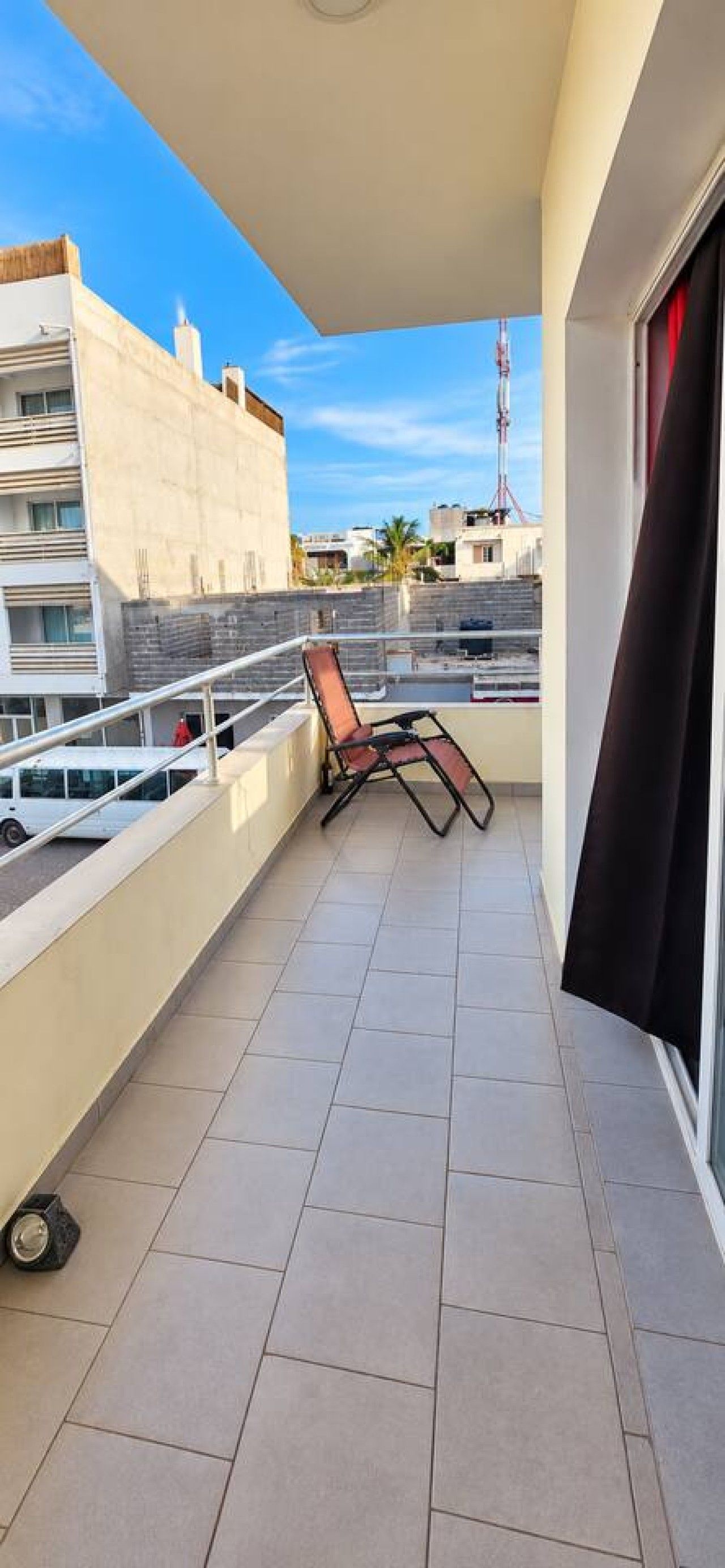 Un balcon doté d’un sol carrelé, de deux chaises longues et offrant une vue sur les bâtiments environnants.