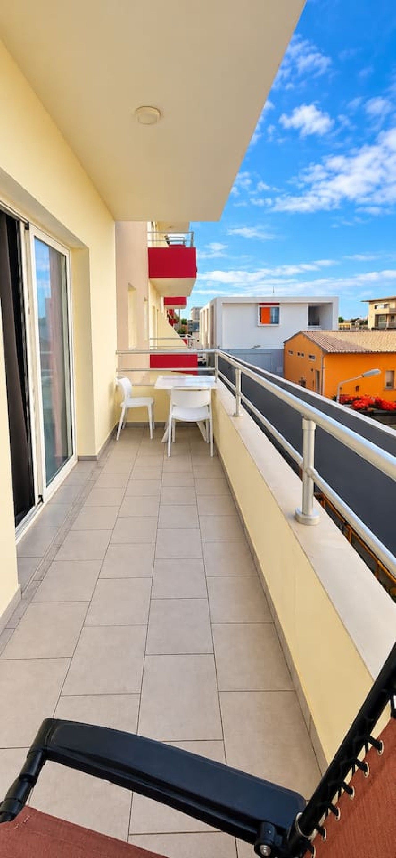 Ein Balkon mit Tisch und Stühlen, einem roten Geländer und Blick auf den Himmel und Gebäude.