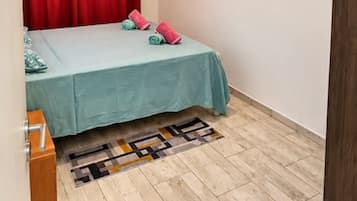 Un dormitorio con una cama, una cortina roja, suelo de color claro y una puerta de madera.