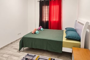 Un dormitori petit i ben organitzat amb un llit individual, una taula de nit i una petita taula auxiliar.
