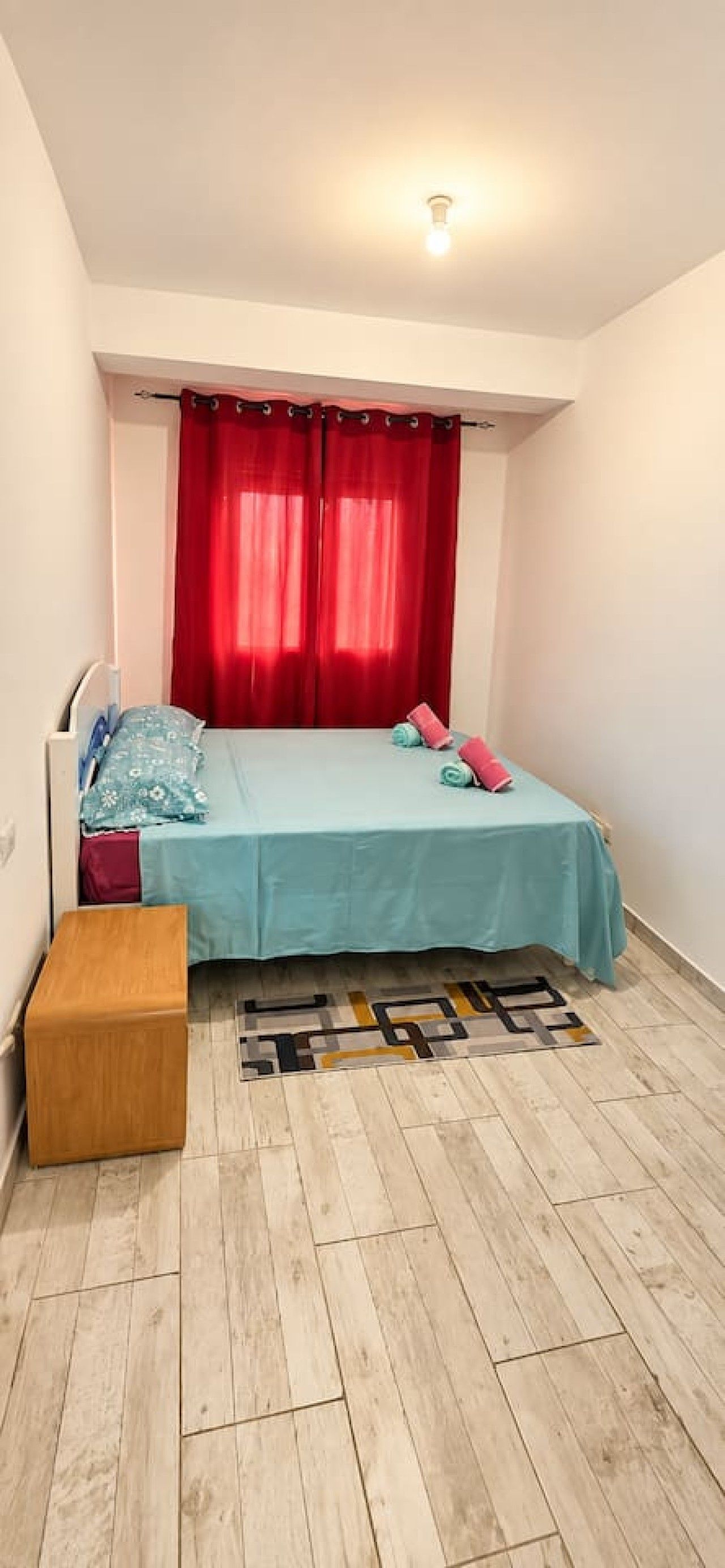 A small, neatly arranged bedroom with a bed, a bench, and a rug.