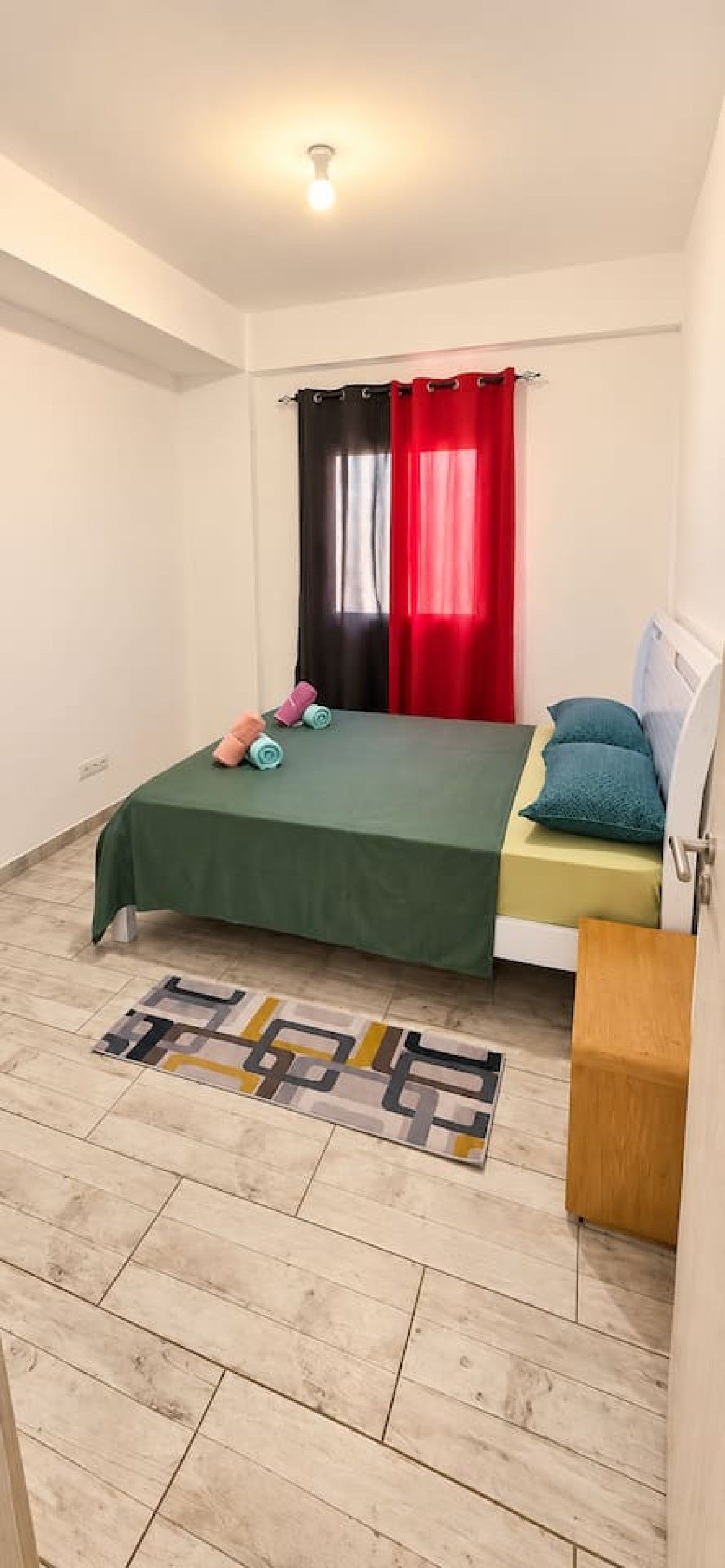 Une chambre à coucher avec un lit, une table de chevet, une fenêtre avec des rideaux et une lampe de sol.