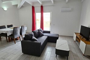 A modern living room with a sectional sofa, a dining table with chairs, a TV stand, and a sliding glass door. - Insuited Penthouse with Rooftop in Estoril beach (Sal Rei)
