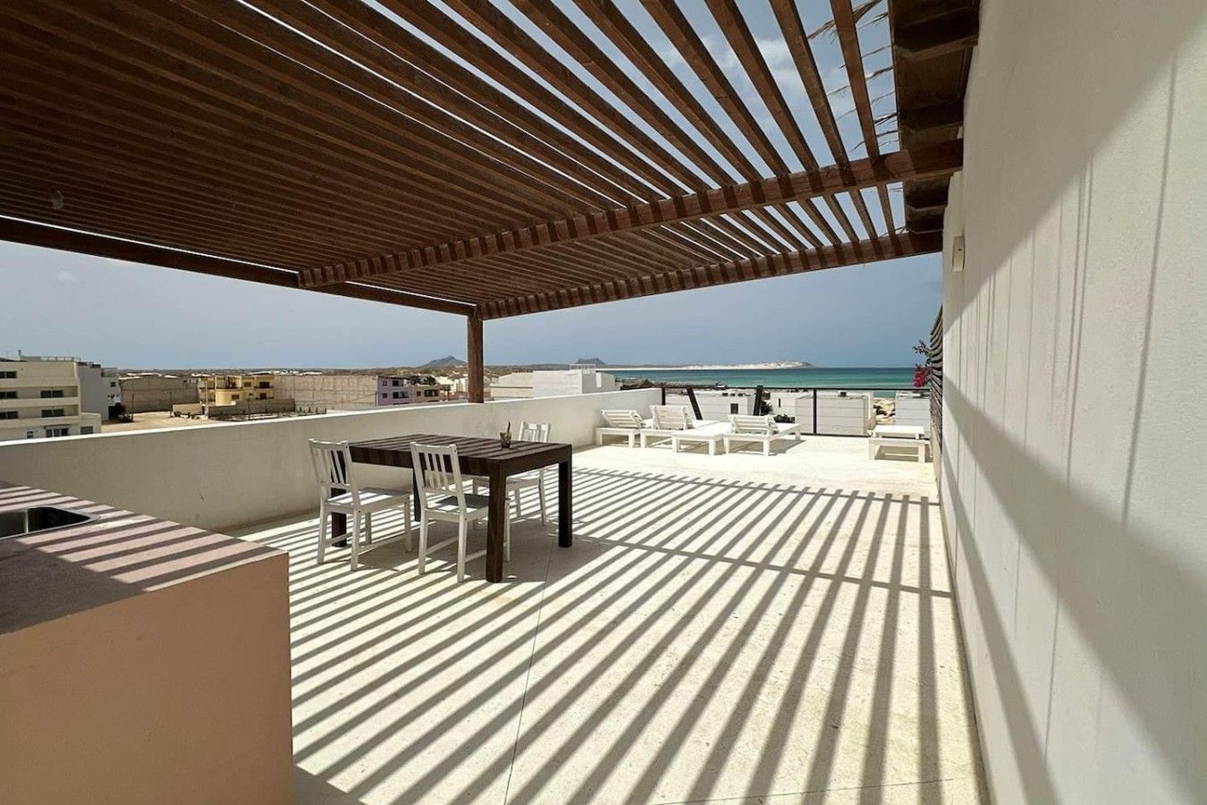 A rooftop terrace with a wooden pergola, a dining table with chairs, and a view of the sea.