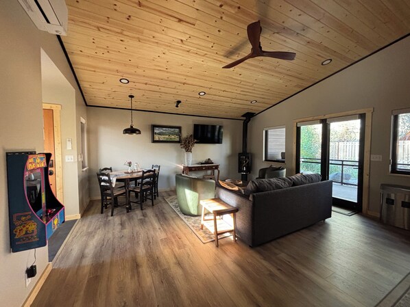 A spacious living area with a wooden ceiling, a sofa, a dining table with chairs, and a television mounted on the wall. - Mountain-modern vacation rental with Full Kitchen, King Bed, Fireplace, Hot Tub (Winthrop)