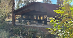 A cabin with a covered patio, large windows, and a view of the surrounding forest. - Mountain-modern vacation rental with Full Kitchen, King Bed, Fireplace, Hot Tub (Winthrop)