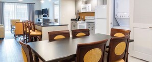 A modern kitchen with white appliances, a dining area with wooden chairs, and a view of the outside through large windows. - Theme park capital of the world! 2 bedroom, two bath, peaceful retreat (Orlando)