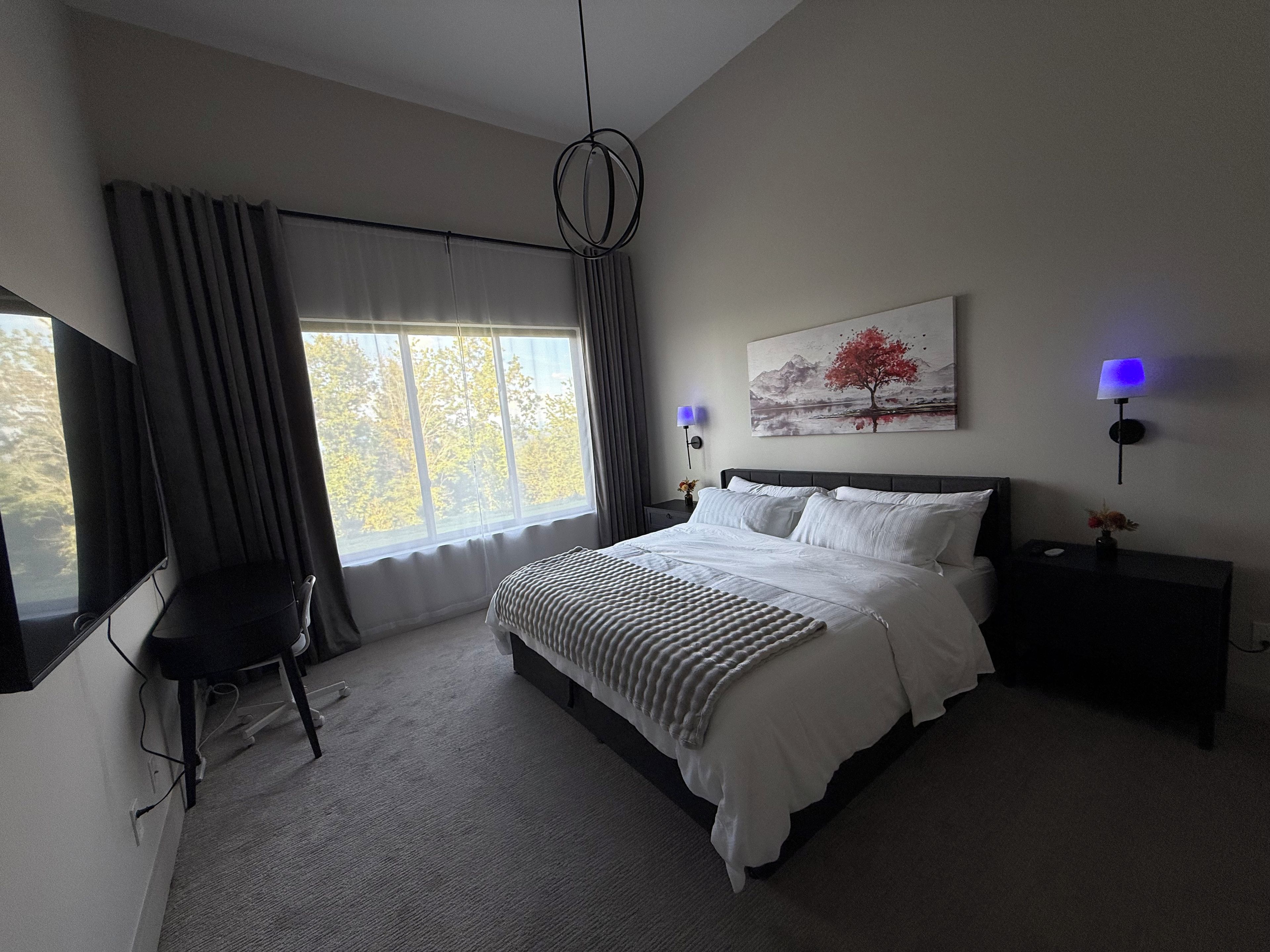 A modern bedroom with a large bed, a desk, and a window with curtains.